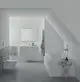 Moderne Badezimmeransicht mit einem Waschbecken und einer Armatur von Ideal Standard. Graue Fliesen, eine Badewanne und ein kleiner Tisch mit Pflegeprodukten sind sichtbar.
